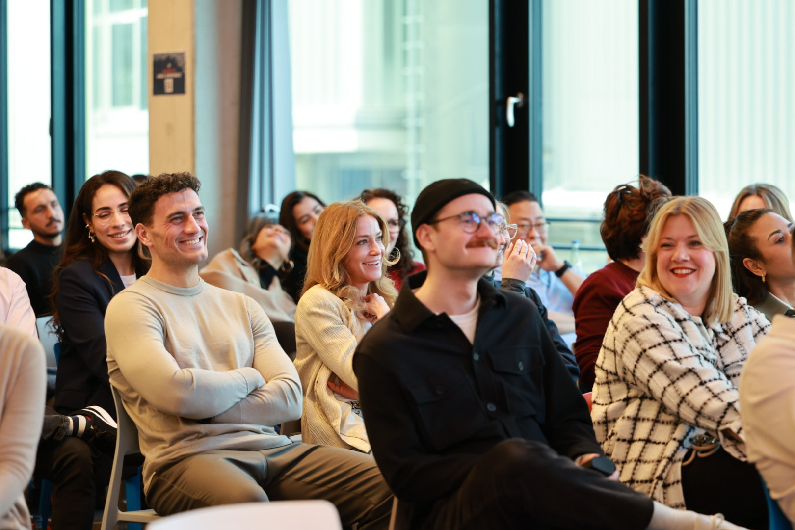 A client team seated in rows in daylight, smiling and listening during an AI Operator session in Munich.