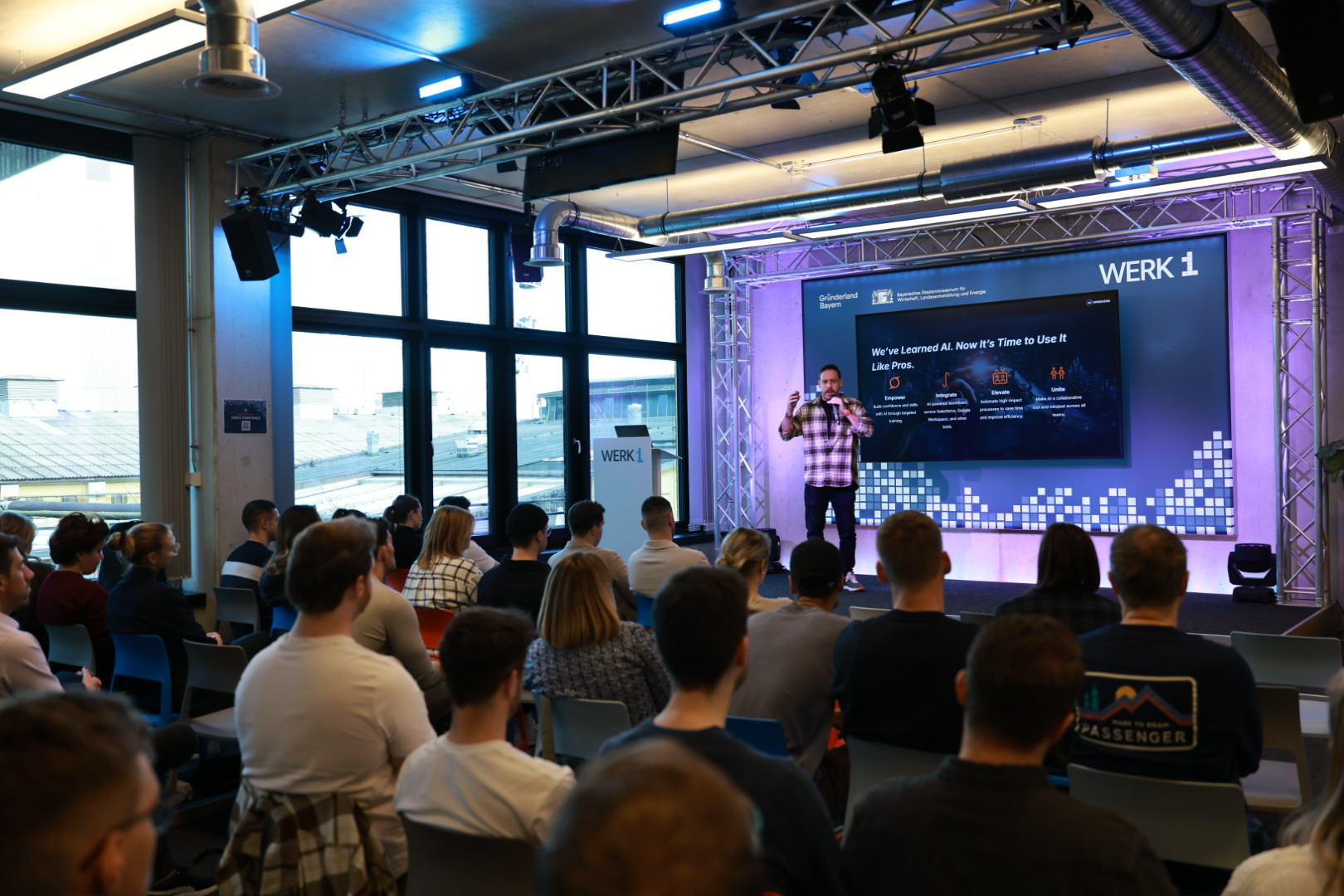 A client leadership team seated in rows facing Tim Cakir on stage at WERK1 in Munich, seen from the back of the room.