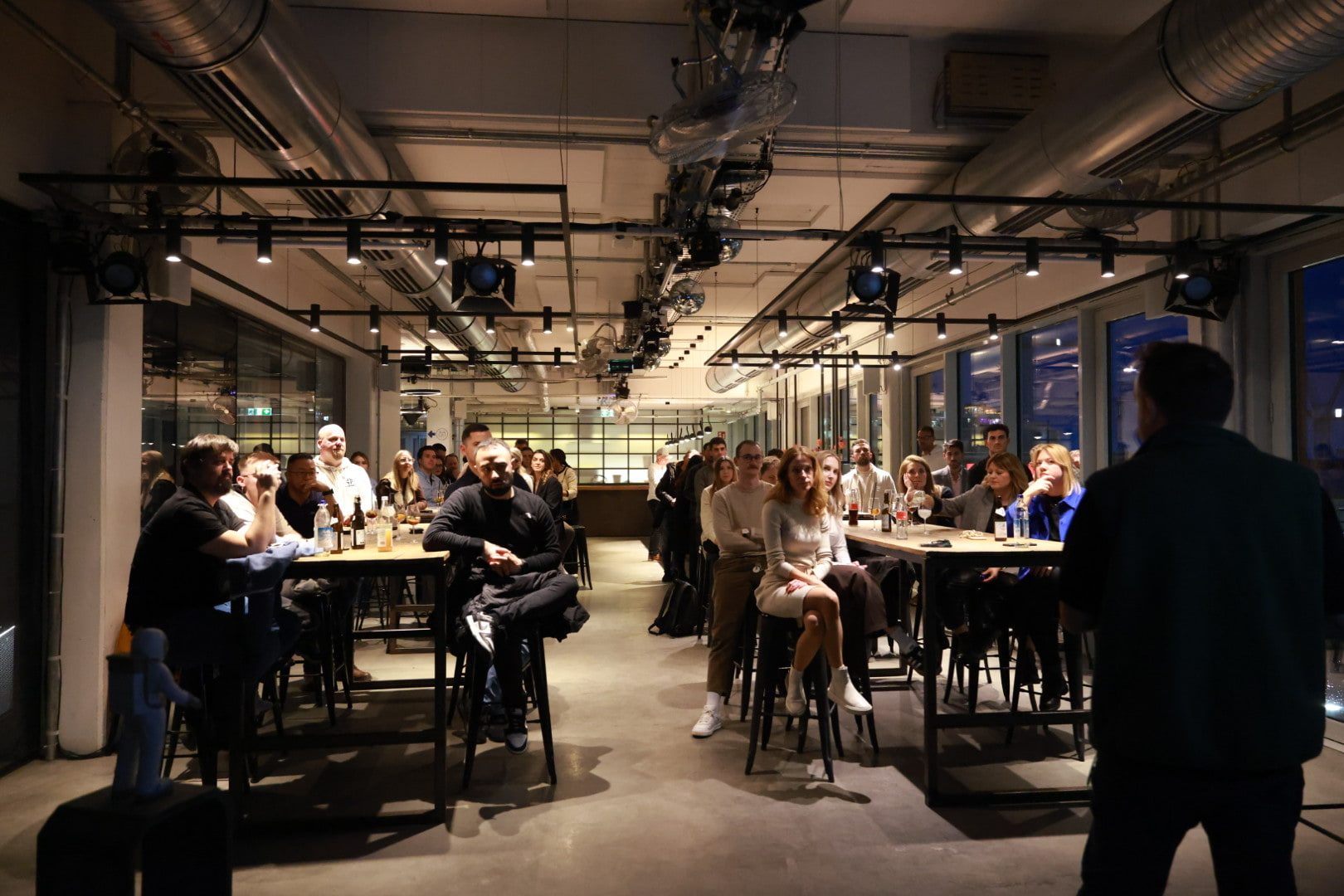A full room of client team members seated at long tables listening during an AI Operator session at WERK1 in Munich, with Tim Cakir's shoulder in the foreground.